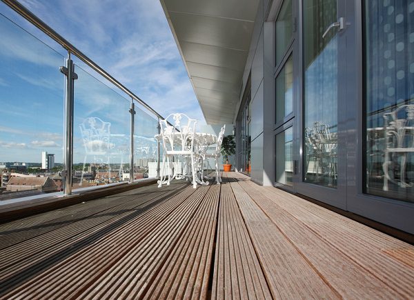 Penthouse apartment balcony with chrome and glass railings and views over city.