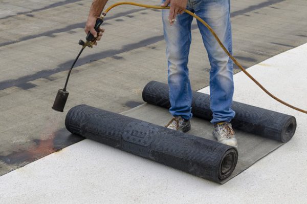 Worker preparing part of bitumen roofing felt roll for melting by gas heater torch flame